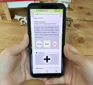 Symbolbild Kindesschutz-App KiSchu: Hände halten ein Smartphone, das App-Oberfläche zeigt