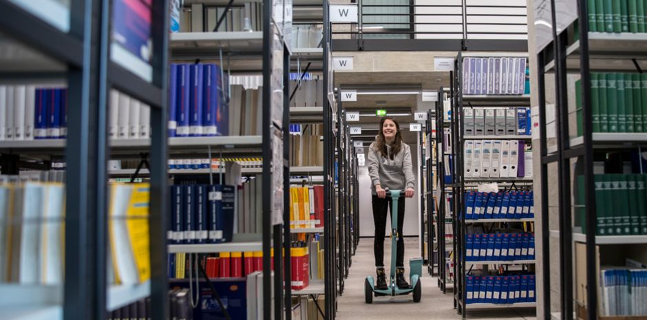 Studentin fährt auf einem Ninebot durch die Bibliothek
