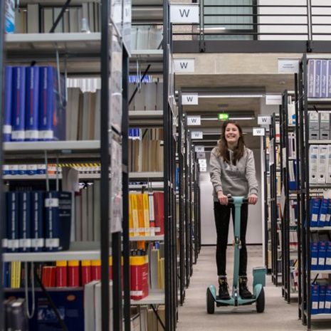 Studentin fährt auf einem Ninebot durch die Bibliothek