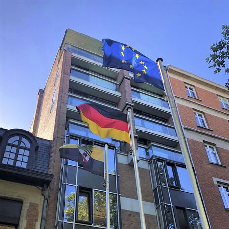 Foto der deutschen und europäischen Flagge vor einem Verwaltungsgebäude.