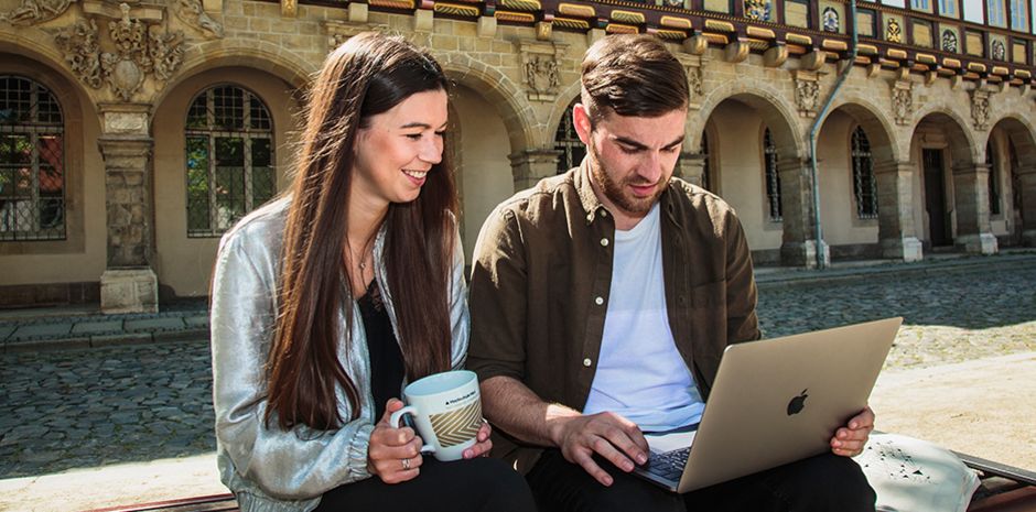 Zwei Studierende des Studiengangs Öffentliche Verwaltung mit Laptop auf dem Domplatz in Halberstadt.
