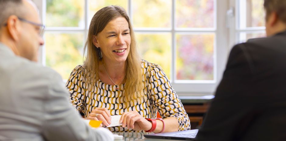 Eine Frau sitzt an einem Tisch und ist im Gespräch mit zwei weiteren Personen