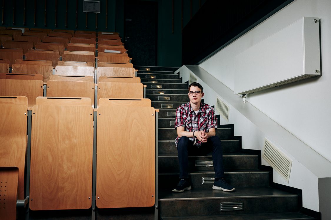 Studierender des Fachbereichs Verwaltungswissenschaften sitzt auf Treppen im Hörsaal und schaut in die Kamera.