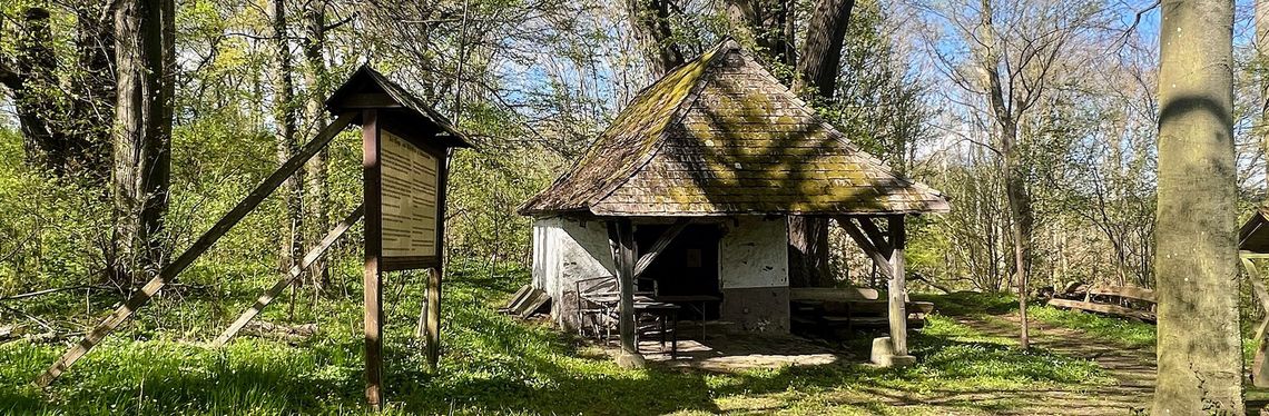 Orte des Rechts: Kleine Hütte im Grünen. Davor zu sehen eine Informationstafel..