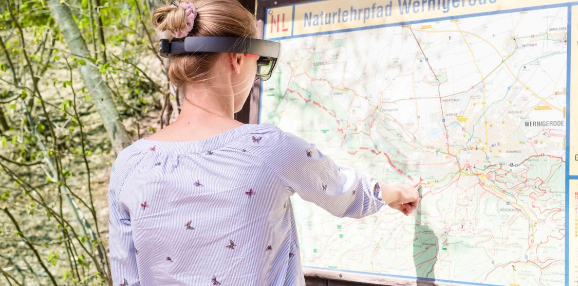 Symbolbild Tourismusforschung an der Hochschule Harz: Junge Frau mit Hololens zeigt auf Wanderkarte
