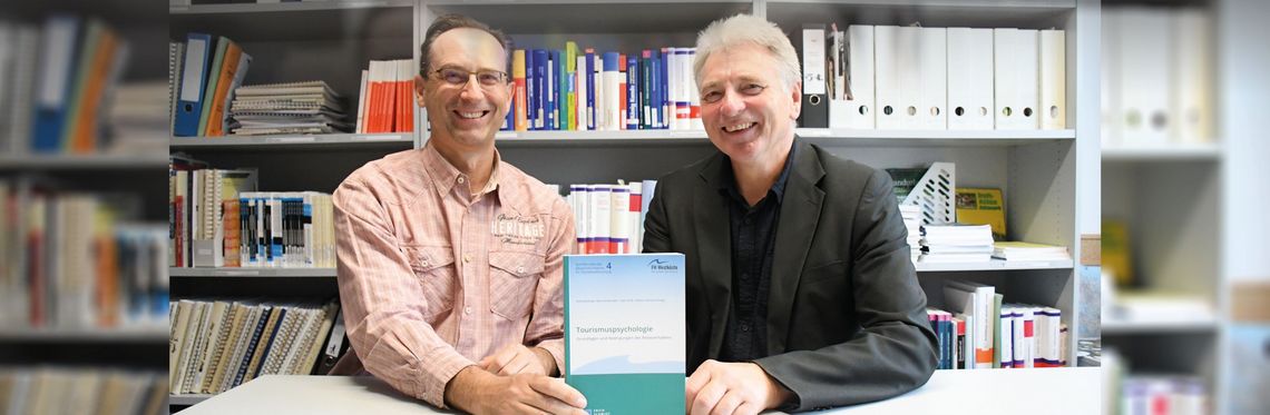Prof. Dr. Sven Groß (li.) und Prof. Dr. Georg Felser sind zwei von vier Autoren der Hochschule Harz, die an dem Sammelband „Tourismuspsychologie – Grundlagen und Bedingungen des Reiseverhaltens“ mitgewirkt haben. Foto: Karoline Klimek Zwei Männer sitzen an einem Tisch, sie halten ein Buch in den Händen. Im Hintergrund ist ein Bücherregal zu sehen.