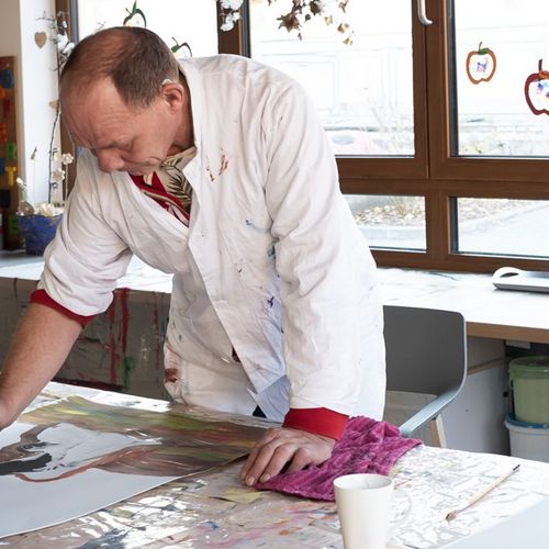 Ein Teilnehmer des Malwerks bei der Arbeit an einem der vorproduzierten Fotografien in einem großen hellen Raum.