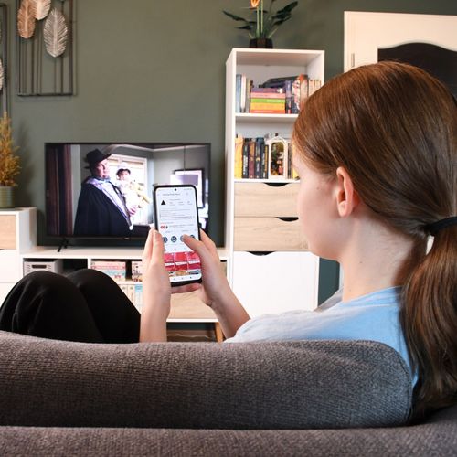 Ein Teenager-Mädchen sitzt vor dem laufenden Fernseher, sie bedient parallel ein Smartphone.