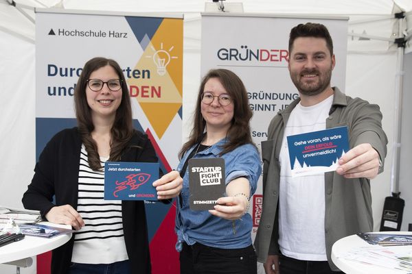 Drei Personen am Infostand lächeln in die Kamera
