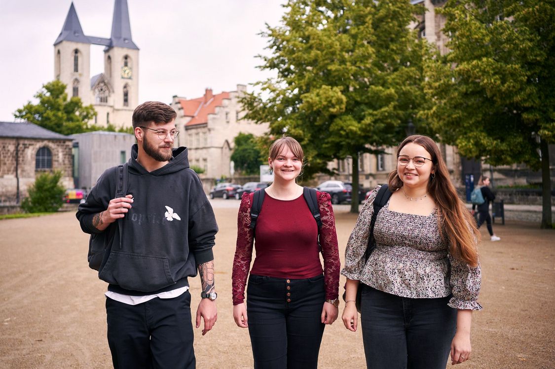Drei Studierende der Verwaltungsökonomie vor dem Hauptgebäude der Hochschule Harz. Sie gehen auf dem Domplatz in Halberstadt.