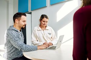 Zwei Studierende des Masterstudiengangs Public Management sitzen in einem modern aussehenden Raum vor großflächigen blauen Bildern.
