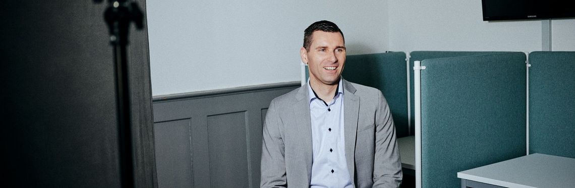 Panoramabild von Prof. Dr.-Ing. Marcus Schmidt vor einer Wand mit brauner Holzvertäfelung im Konferenzraum des Fachbereichs Verwaltungswissenschaften der Hochschule Harz