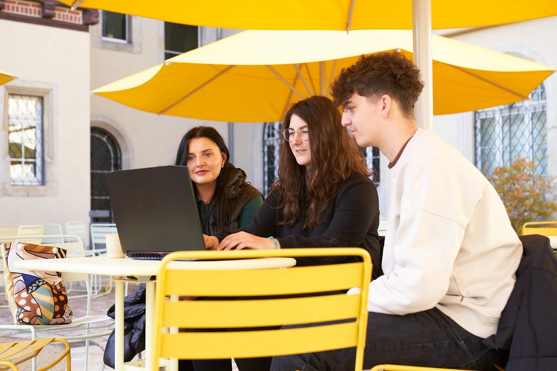 Drei Studierende des IT-Managements –  Verwaltungsinformatik sitzen vor einem Laptop im neu gestalteten Innenhof der Hochschule Harz am Standort Halberstadt.