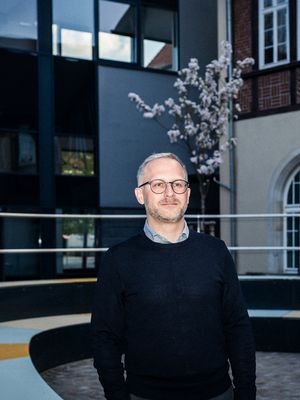 Porträt von Dr. Christian Gläßel im Innenhof der Hochschule Harz. Angeblitzt in den Abendstunden, im Hintergrund ein blühender Baum.