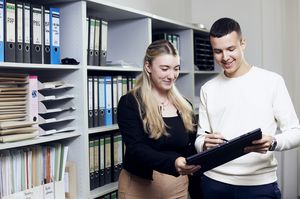 Zwei Studierende stehen vor einem Bücherregal una halten ein Tabelt in der Hand.