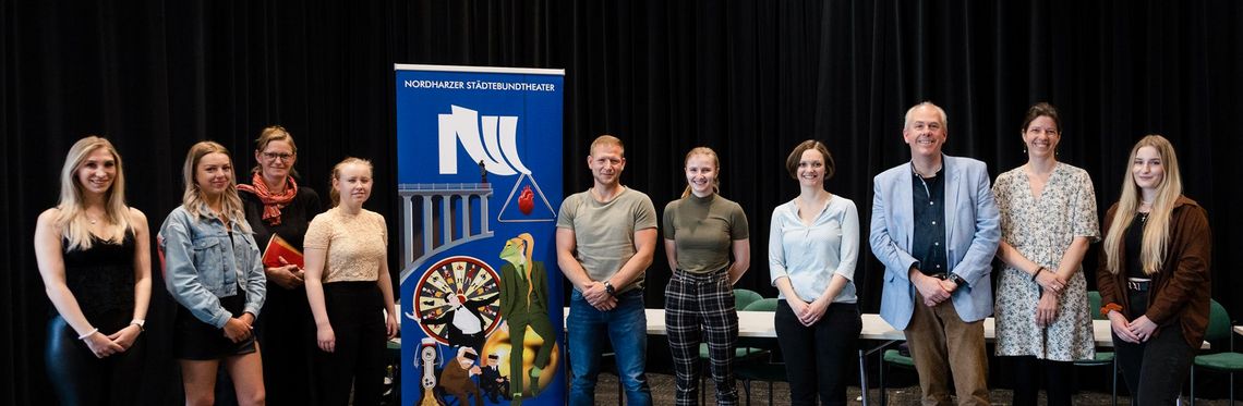 Gruppenbild von Studierenden der Hochschule Harz und Mitarbeitenden des Nordharzer Städtebundtheaters beim Pressetermin vor schwarzem Hintergrund