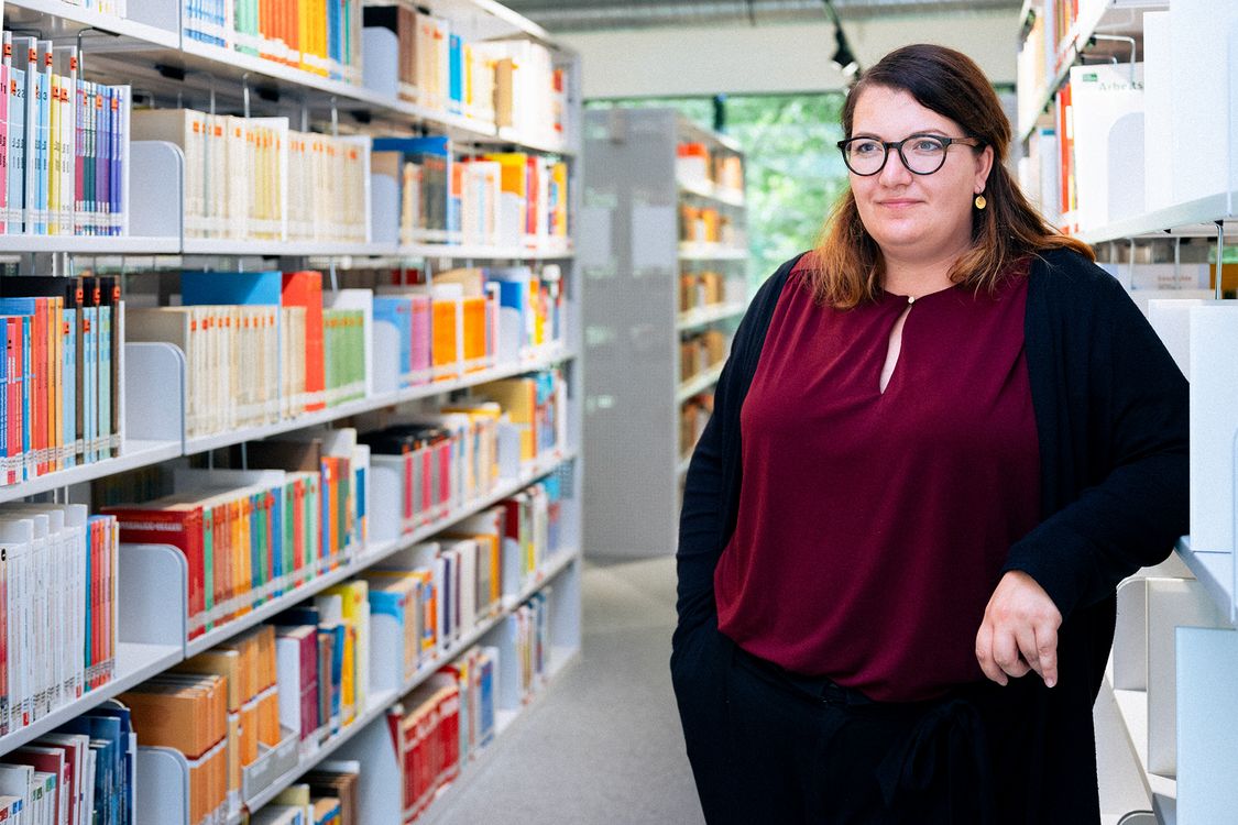 Absolventin der Verwaltungsökonomie vor einer Reihe von Büchern in einer großen, hellen Bibliothek.