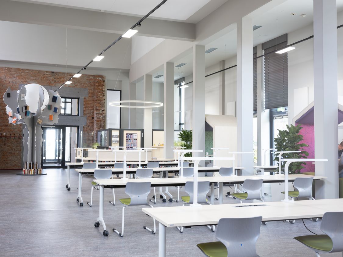 Blick in die neu eröffnete Hochschulbibliothek mit modernen Arbeitsplätzen, dem Kunst-am-Bau-Projekt "Baum-des-Wissens" und beleuchteter Ausgabe. 