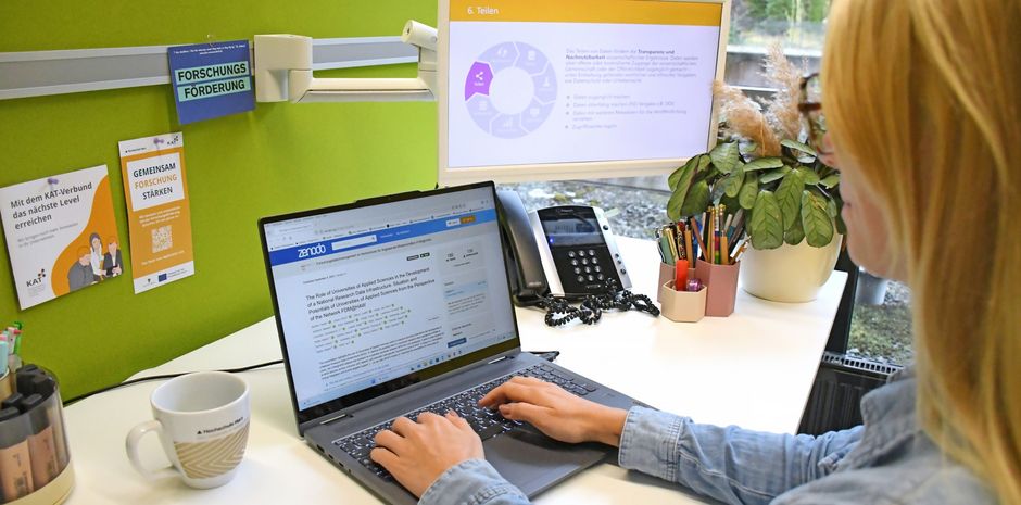 Eine Person sitzt an einem Schreibtisch, sie arbeitet an einem Laptop.