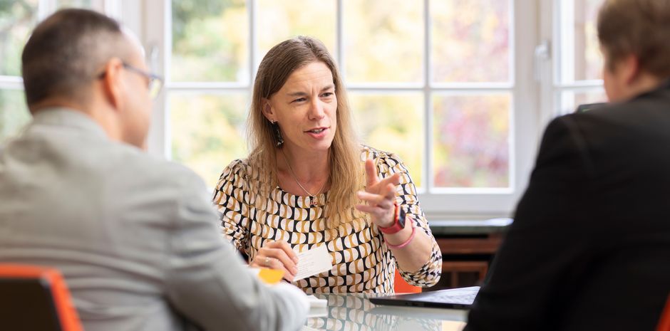 Eine Frau sitzt an einem Tisch und ist im Gespräch mit zwei weiteren Personen