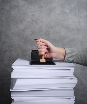 Hand mit Stempel auf einem Stapel Papier.