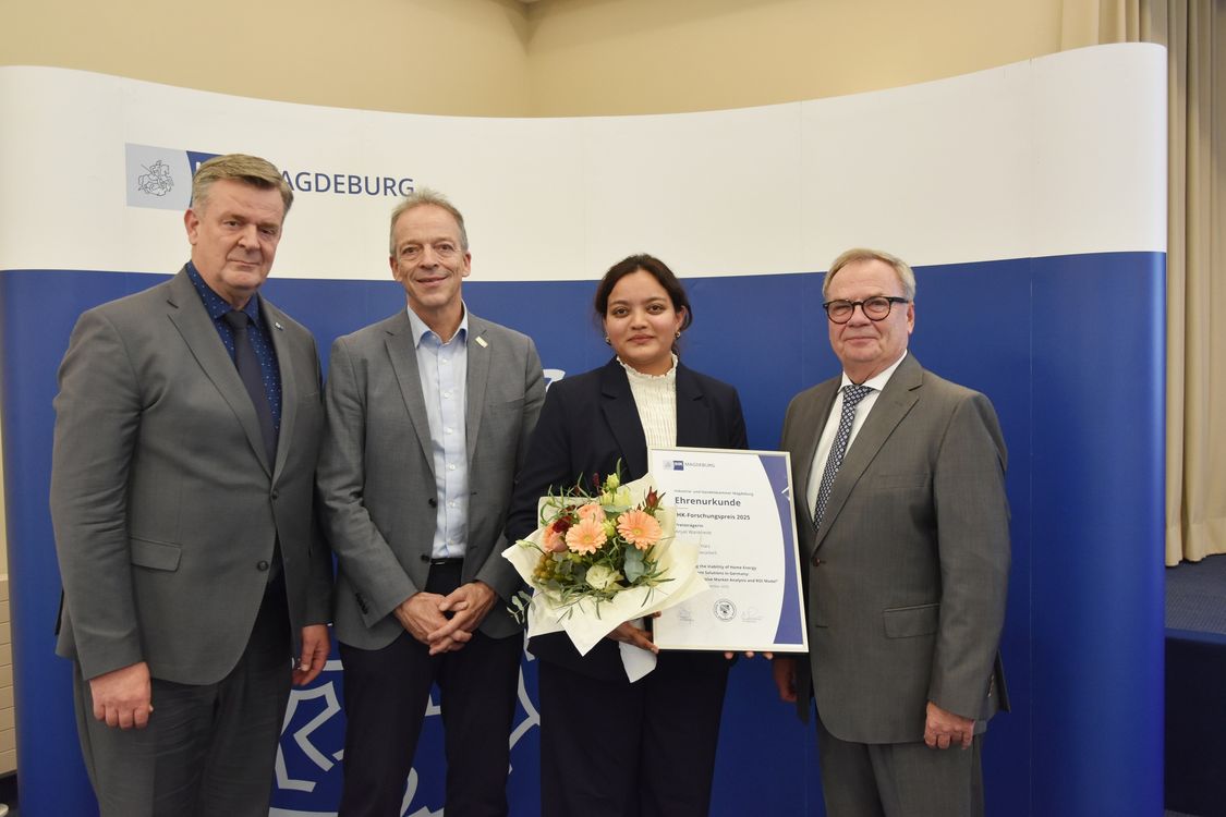 Four people stand in a row, award winner holds certificate and flowers in her hand.