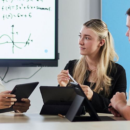 Vier Studierende des Masterstudiengangs Digitale Verwaltung mit Tablet vor einem hell strahlendem Whiteboard.