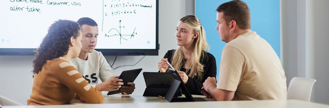 Vier Studierende des Masterstudiengangs Digitale Verwaltung mit Tablet vor einem hell strahlendem Whiteboard.