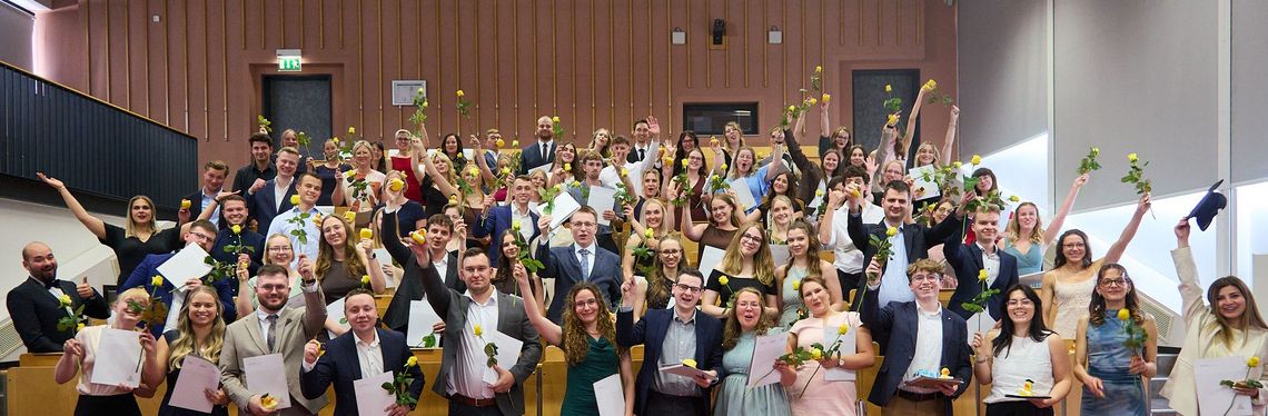 Absolventen des Fachbereichs Verwaltungswissenschaften im Hörsaal jubeln über ihren erfolgreichen Abschluss.