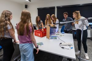Raum mit einer Gruppe von Personen, die um einen Tisch mit Utensilien zur Cyanotypie-Entwicklung stehen und diskutieren.