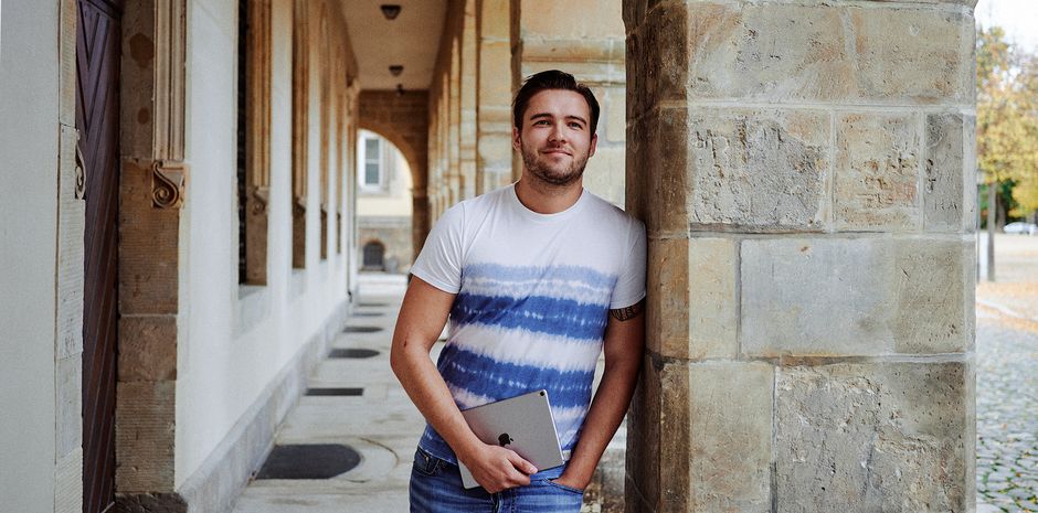 Ein Student des Public Management im Kreuzgang vor dem Fachbereich Verwaltungswissenschaften schaut direkt in die Kamera.