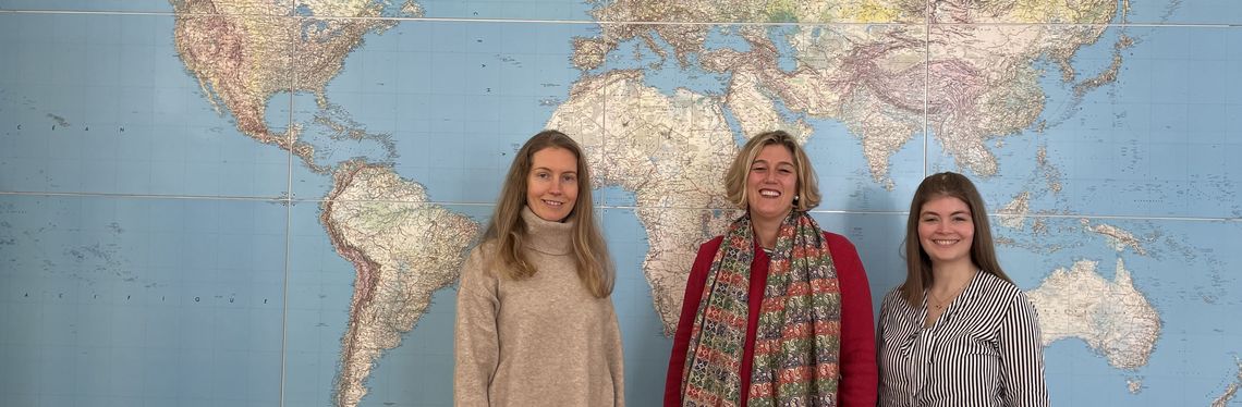 Bild mit drei Frauen vor einer Weltkarte zeigt das Team der "International Research Week" der Hochschule Harz