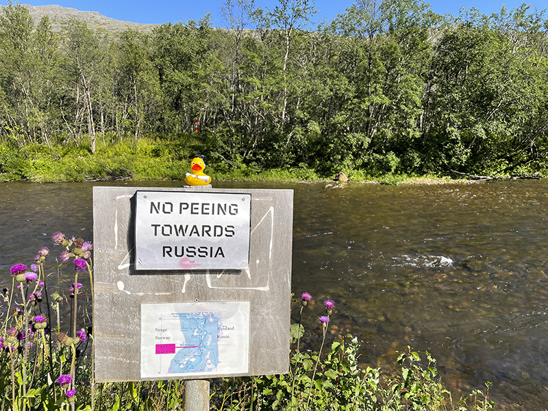 Plastikente auf Holzschild an der Grenze von Norwegen und Russland.