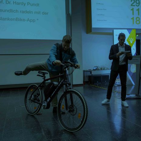 Symbolbild Virtuelle Thementage Hochschule Harz Präsentation Forschung Bühne mit einem Mann auf dem Fahrrad und Moderator